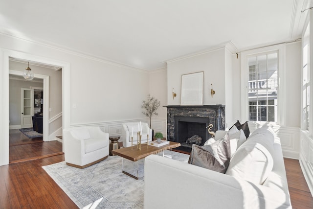 living room with crown molding, a fireplace, dark wood finished floors, a decorative wall, and wainscoting