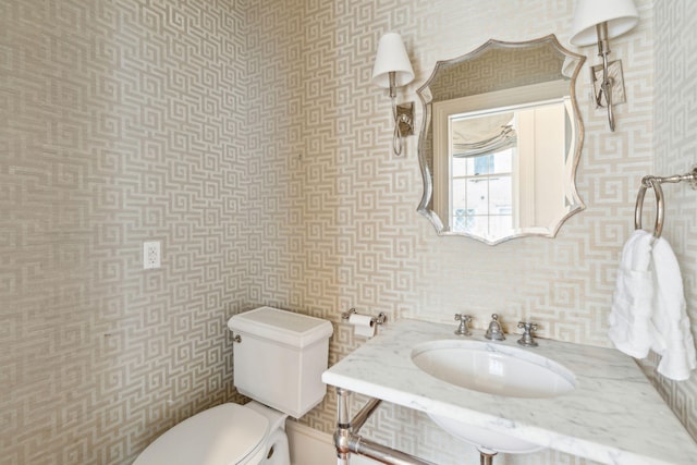 half bath with a sink, toilet, and wallpapered walls