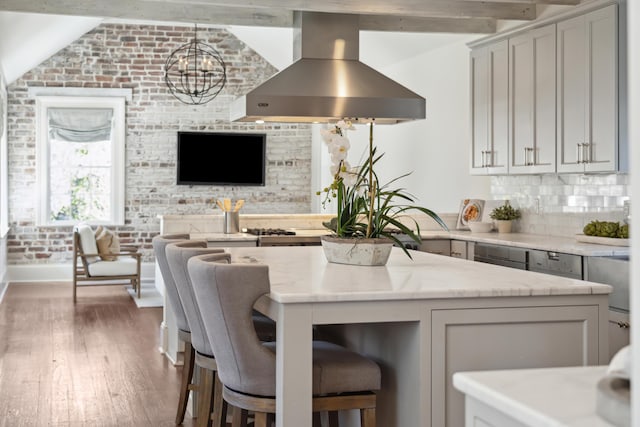 kitchen featuring dark wood-style floors, brick wall, light stone countertops, range hood, and gray cabinetry