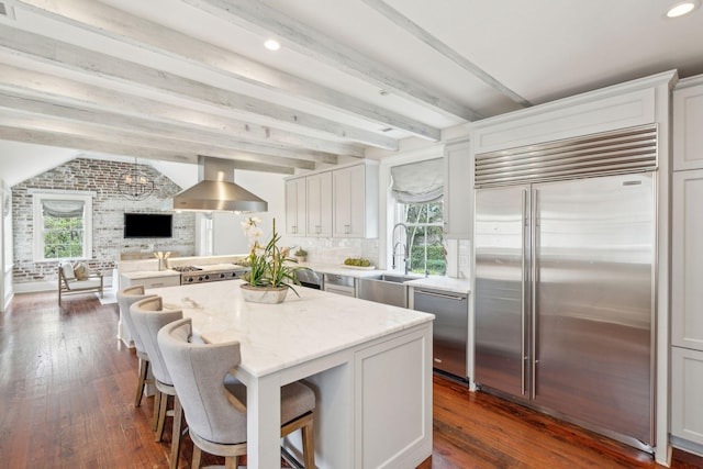 kitchen featuring appliances with stainless steel finishes, open floor plan, a sink, wall chimney range hood, and a kitchen island