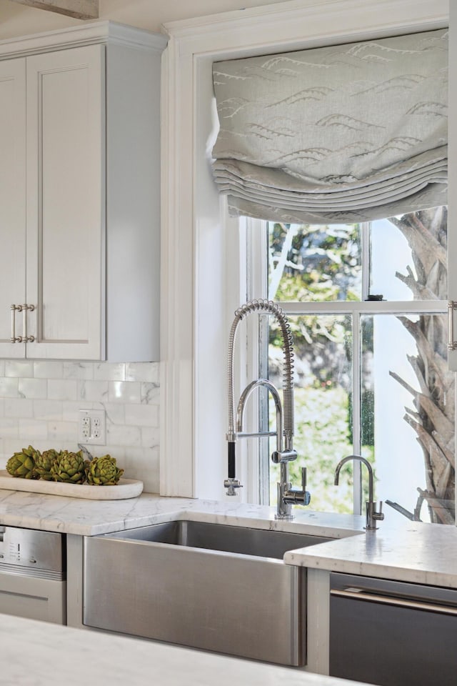 kitchen featuring a sink, white cabinets, black dishwasher, light countertops, and decorative backsplash