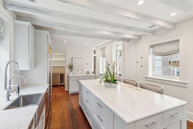 kitchen with light stone counters, beverage cooler, dark wood-style flooring, a sink, and a kitchen island