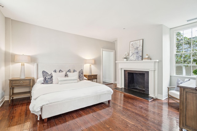 bedroom featuring dark wood-type flooring, visible vents, a fireplace with raised hearth, and baseboards