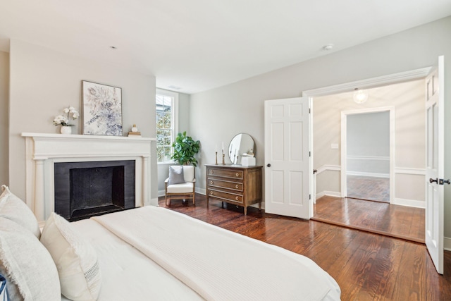 bedroom featuring a fireplace, dark wood finished floors, and baseboards