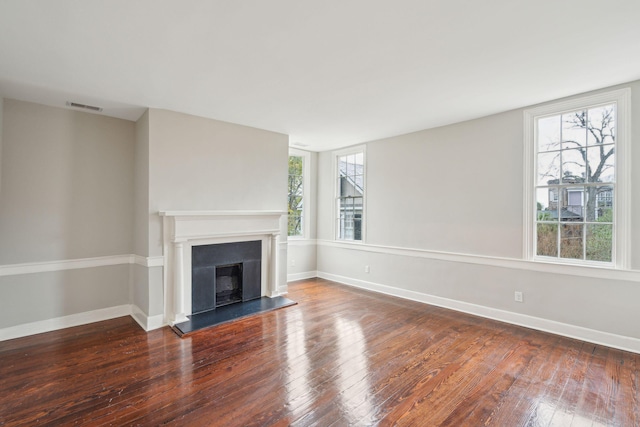 unfurnished living room featuring a fireplace with raised hearth, baseboards, and wood finished floors