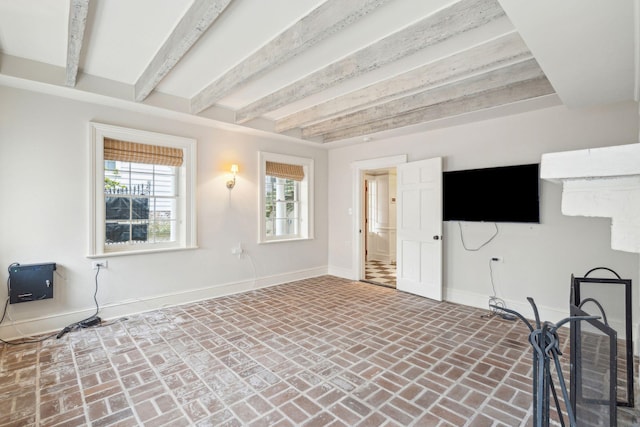 unfurnished living room with beamed ceiling, brick floor, and baseboards