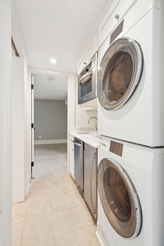 washroom with light tile patterned floors, stacked washer and dryer, laundry area, a sink, and baseboards