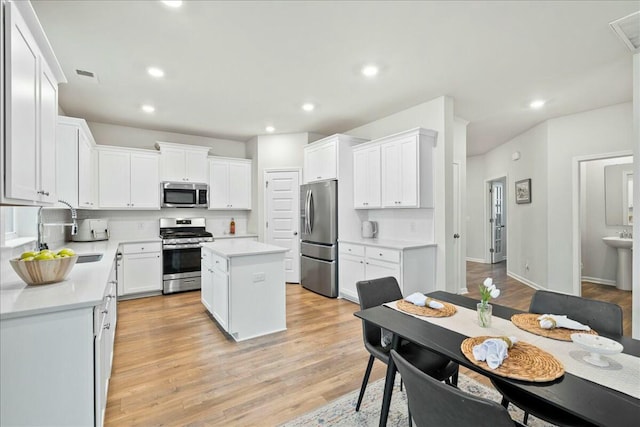 kitchen with appliances with stainless steel finishes, sink, white cabinets, a center island, and light hardwood / wood-style floors