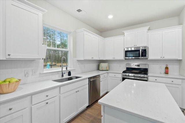 kitchen with tasteful backsplash, appliances with stainless steel finishes, sink, and white cabinets