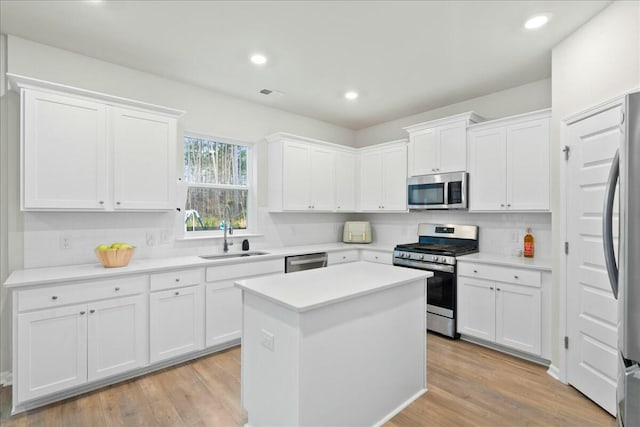 kitchen with stainless steel appliances, a kitchen island, sink, and white cabinets