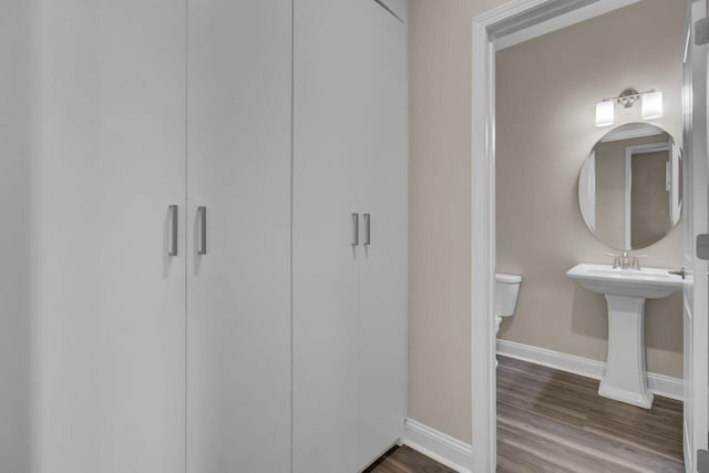 half bathroom featuring toilet, a sink, baseboards, and wood finished floors