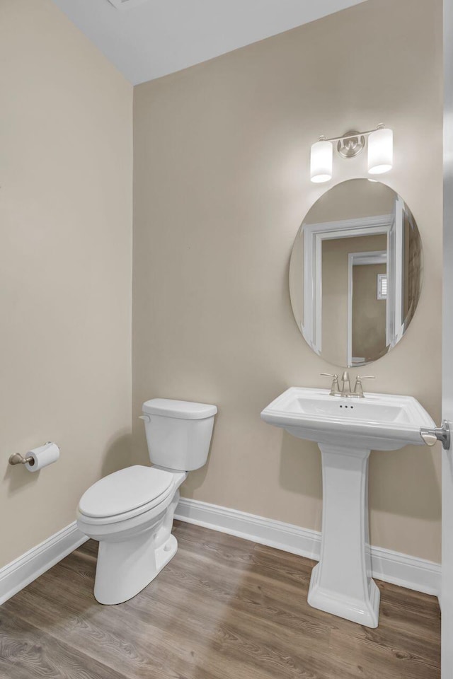 half bath featuring toilet, baseboards, and wood finished floors