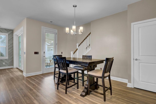 dining space featuring baseboards, wood finished floors, stairs, and a notable chandelier