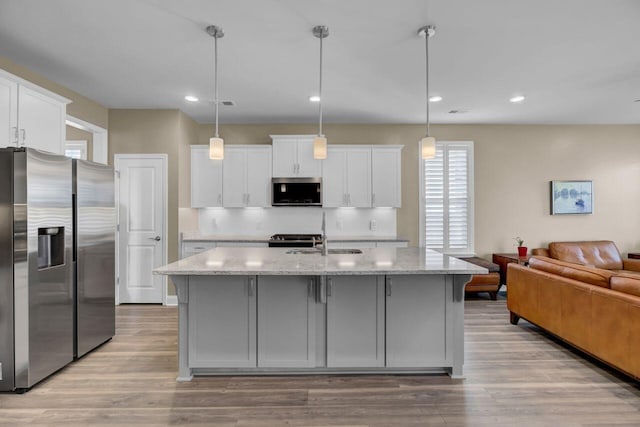 kitchen featuring open floor plan, stainless steel appliances, a sink, and white cabinets