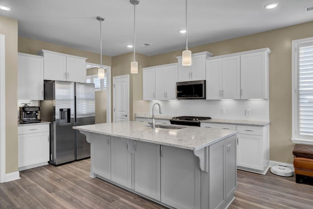 kitchen with stainless steel appliances, wood finished floors, a sink, white cabinets, and tasteful backsplash