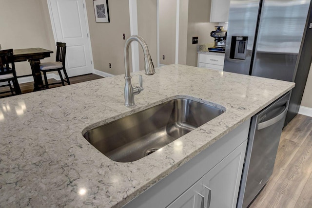 kitchen with light stone counters, stainless steel appliances, light wood-type flooring, white cabinetry, and a sink