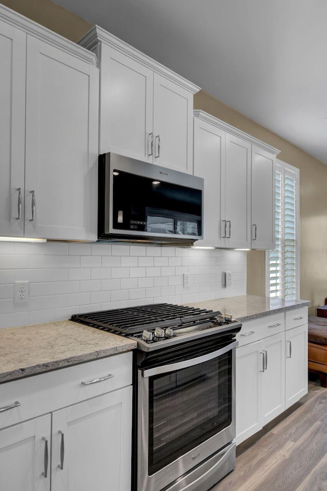 kitchen with light wood-type flooring, white cabinetry, stainless steel appliances, and backsplash