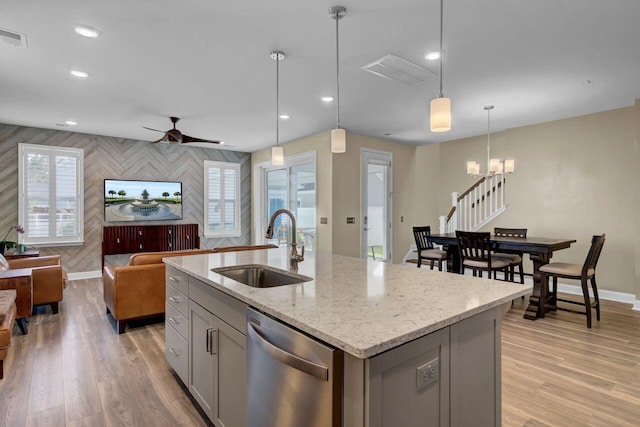 kitchen featuring open floor plan, stainless steel dishwasher, a sink, and gray cabinetry