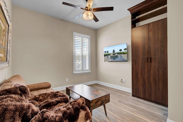 living room featuring baseboards, a ceiling fan, and light wood-style floors