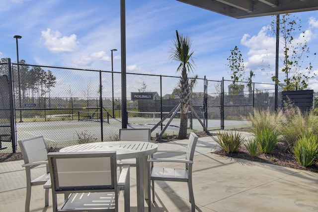 view of patio with a tennis court, outdoor dining space, and fence