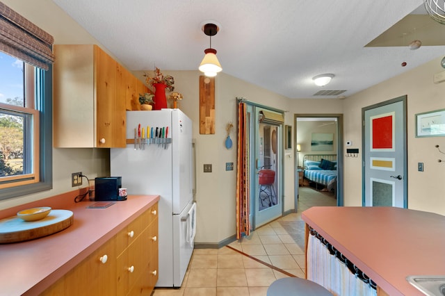 kitchen featuring a textured ceiling, light tile patterned floors, pendant lighting, and white refrigerator