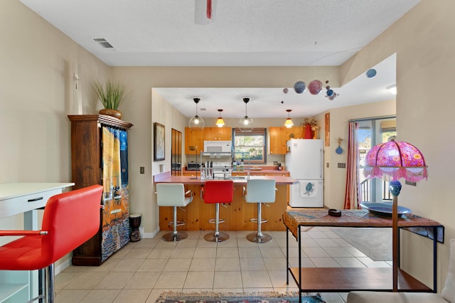 kitchen featuring a breakfast bar area, kitchen peninsula, light tile patterned flooring, pendant lighting, and white appliances