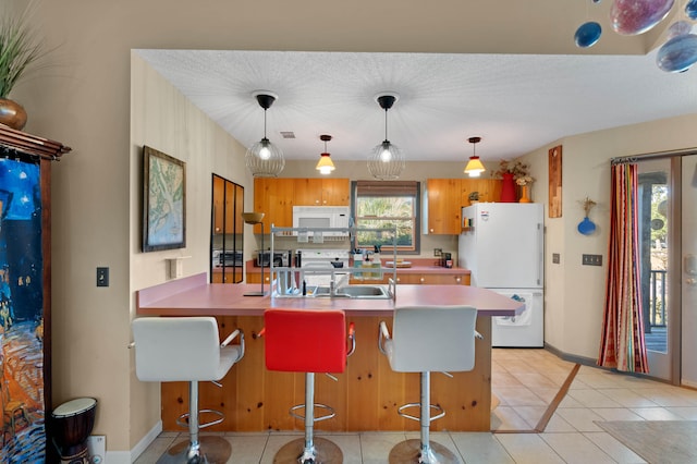 kitchen featuring sink, a breakfast bar, pendant lighting, white refrigerator, and a textured ceiling