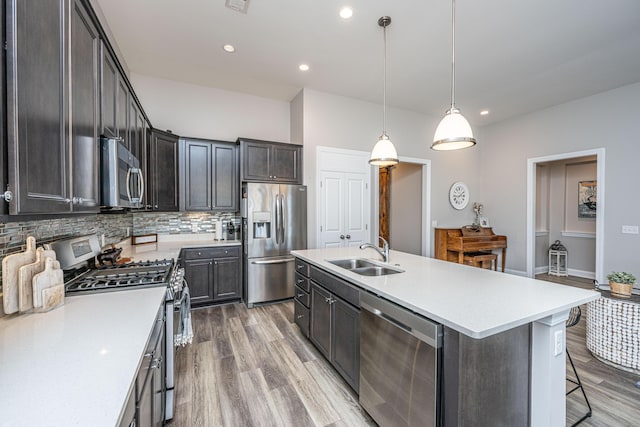 kitchen featuring pendant lighting, sink, stainless steel appliances, an island with sink, and decorative backsplash