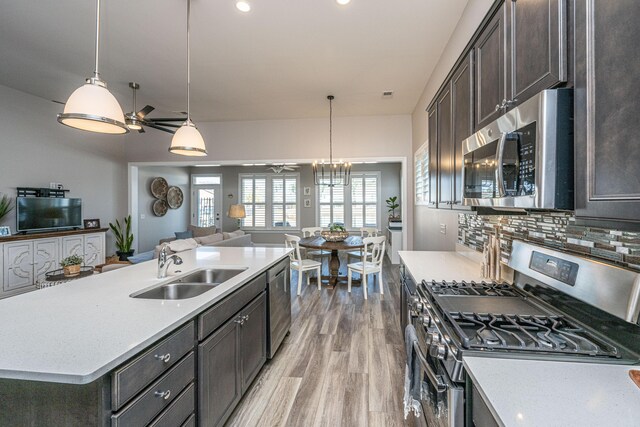 kitchen with appliances with stainless steel finishes, light hardwood / wood-style floors, sink, and hanging light fixtures