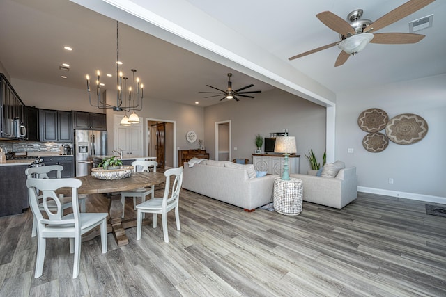 dining space with ceiling fan with notable chandelier and light hardwood / wood-style floors