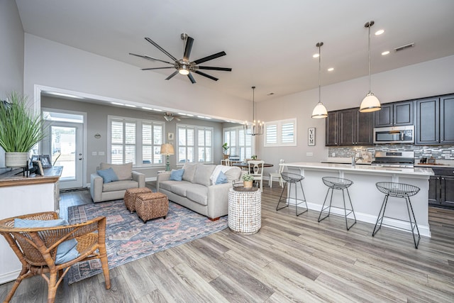 living room featuring ceiling fan with notable chandelier and light hardwood / wood-style flooring