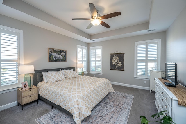 bedroom featuring a raised ceiling, ceiling fan, and dark colored carpet