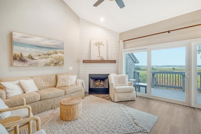 living room featuring ceiling fan, high vaulted ceiling, a large fireplace, and light wood-type flooring