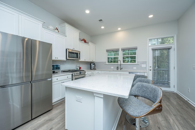 kitchen featuring light hardwood / wood-style flooring, stainless steel appliances, light stone countertops, a center island, and white cabinetry