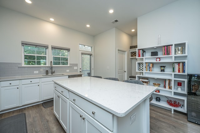 kitchen featuring light stone countertops, sink, a kitchen island, white cabinets, and dark wood-type flooring