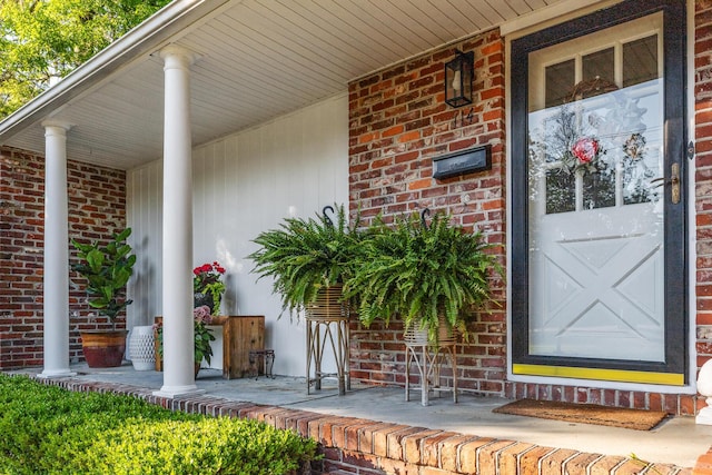 view of exterior entry with brick siding and covered porch