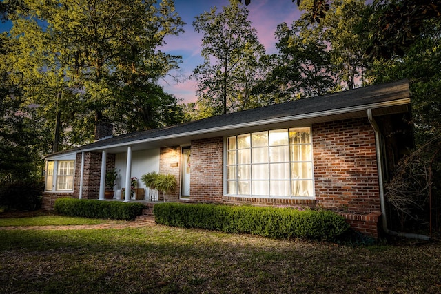 property exterior at dusk with a chimney, a lawn, covered porch, and brick siding