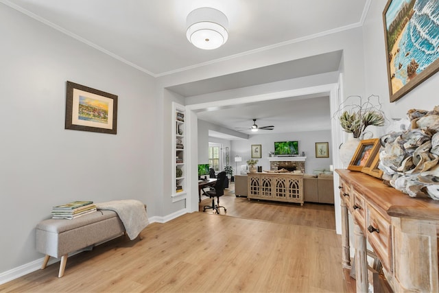 entryway with ornamental molding, a ceiling fan, light wood-style floors, and a fireplace