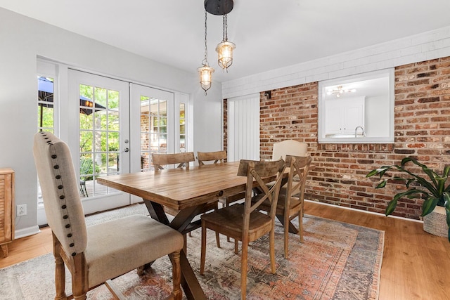 dining space featuring brick wall, french doors, and light wood-type flooring