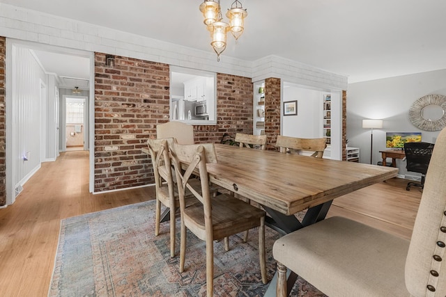 dining space featuring light wood-type flooring, ornamental molding, brick wall, baseboards, and a notable chandelier