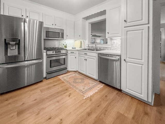 kitchen with appliances with stainless steel finishes, light wood-type flooring, white cabinetry, decorative backsplash, and a sink