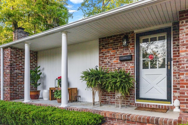 property entrance with a chimney, covered porch, and brick siding