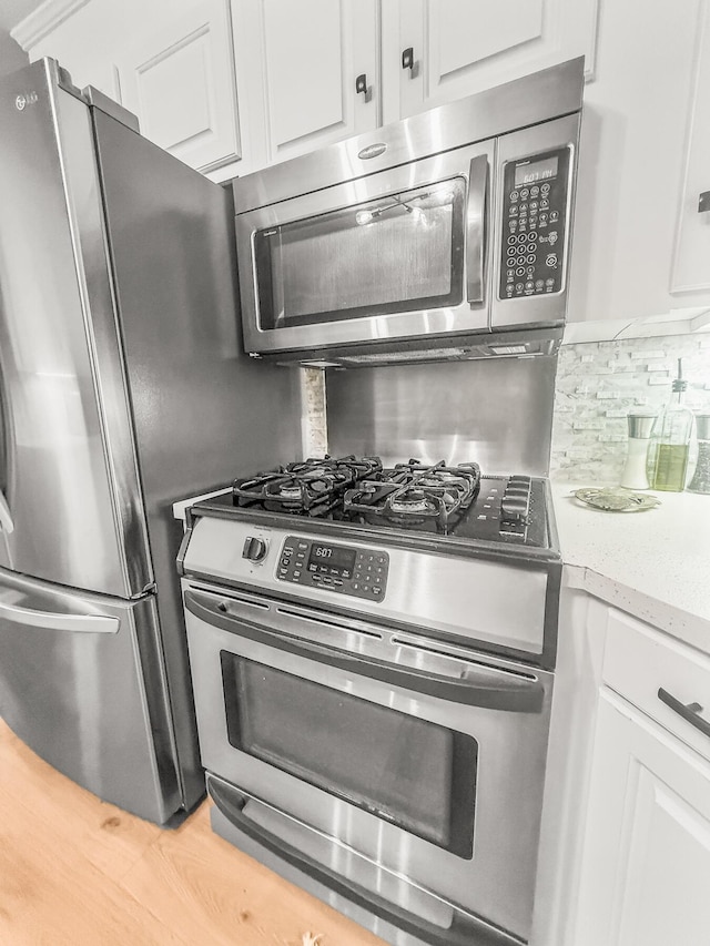 kitchen with light stone counters, backsplash, white cabinets, and stainless steel appliances