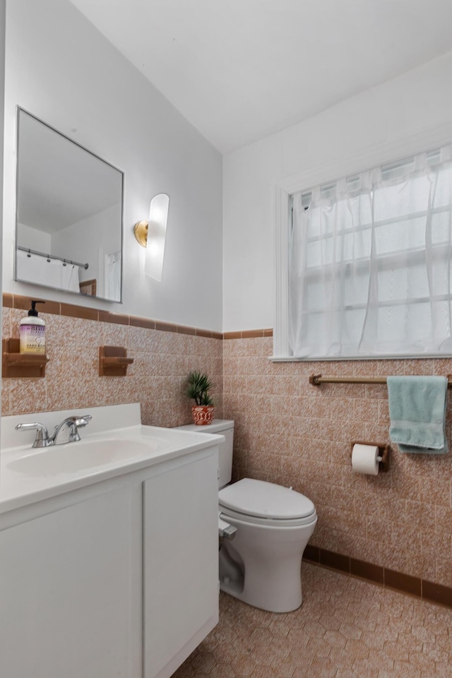 bathroom featuring toilet, tile walls, vanity, and a wainscoted wall
