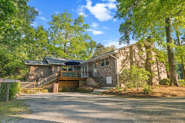 view of front of house featuring brick siding, a wooden deck, stairway, and a chimney