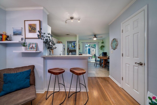 kitchen with kitchen peninsula, a kitchen breakfast bar, crown molding, white refrigerator, and light wood-type flooring