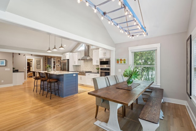 dining room with light wood-type flooring, high vaulted ceiling, and sink