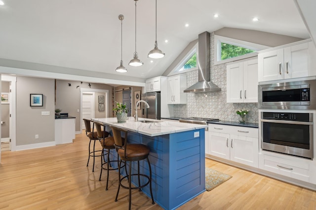 kitchen featuring wall chimney exhaust hood, white cabinetry, stainless steel appliances, and vaulted ceiling