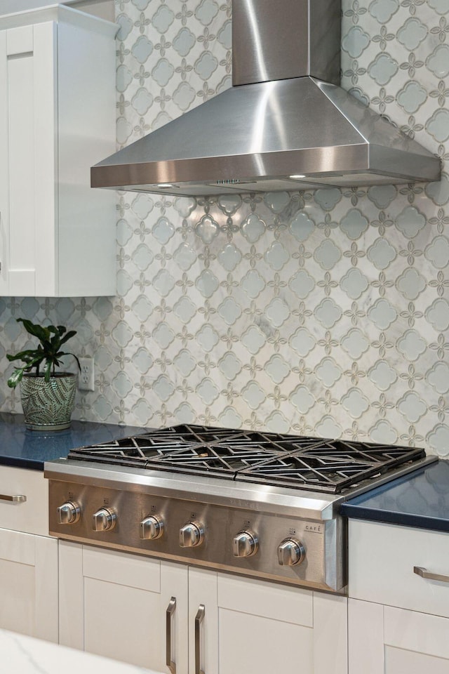 kitchen featuring stainless steel gas stovetop, wall chimney exhaust hood, white cabinetry, and tasteful backsplash