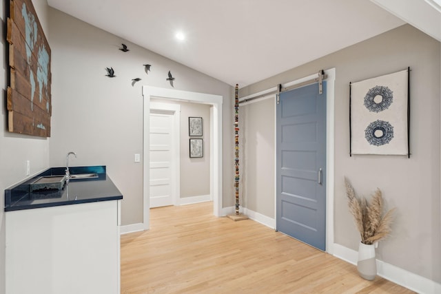 kitchen featuring a barn door, sink, wood-type flooring, and lofted ceiling